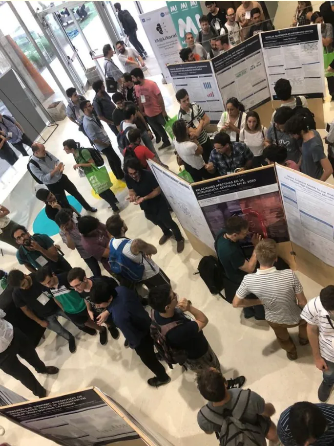 The IA@Litoral 2019 exhibition seen from above, with the poster among the panels and the public walking through
